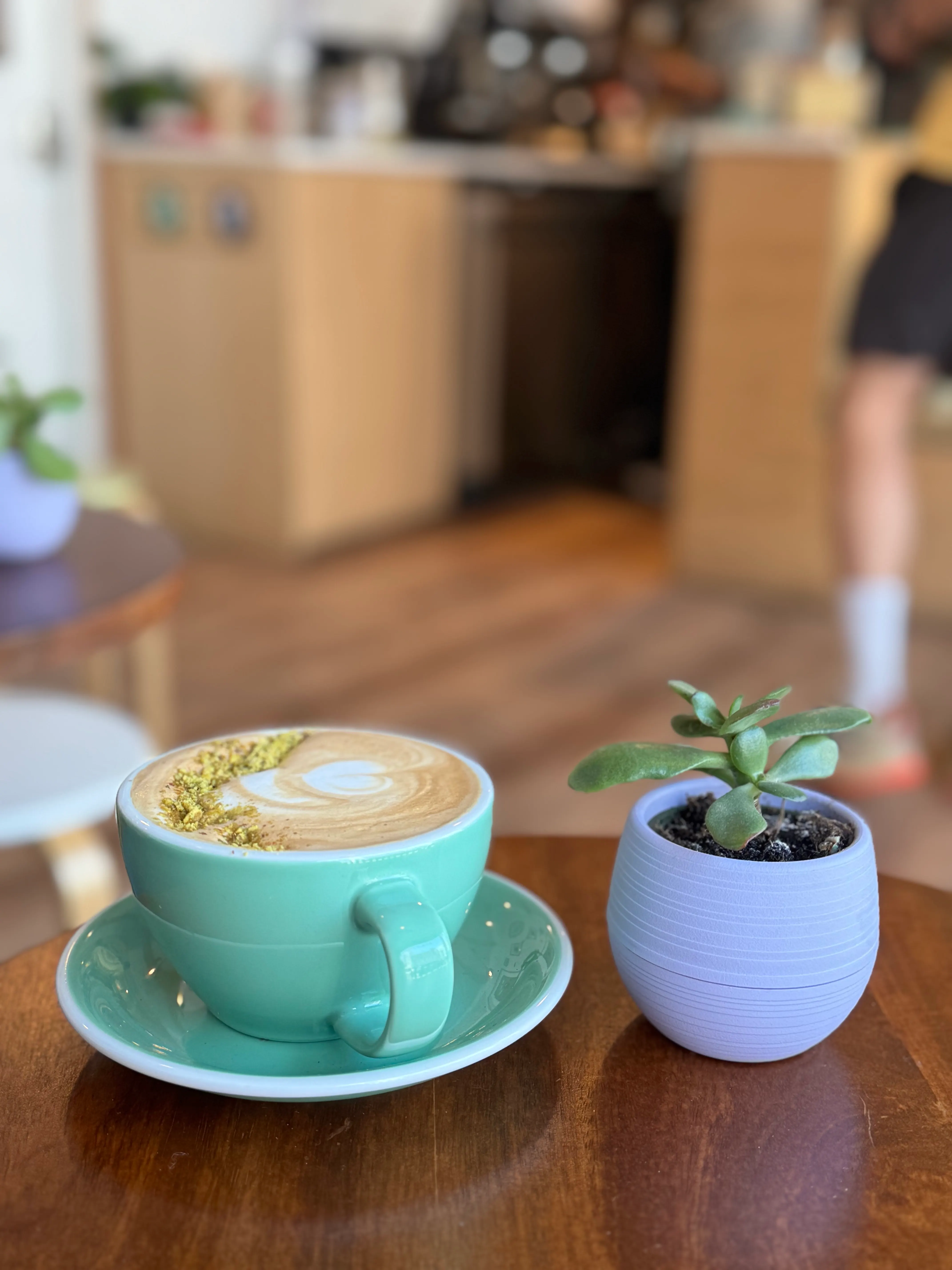 Pistachio latte in a mint cup beside a small potted plant
